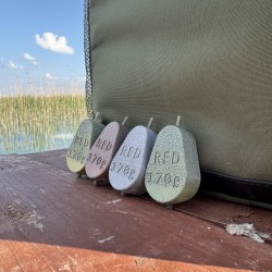 Red Sinker Inline 170 grammos horgász súlyok több színben, természetközeli környezetben a vízparton. Ideális választás pontyozó horgászathoz. Red Sinker Inline horgász súlyok 170g különböző színekben a vízparton