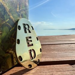 Red Sinker logóval ellátott horgász súly a Balaton partján, természetes háttérrel. Red Sinker logós horgász súly a Balaton partján, stégen elhelyezve